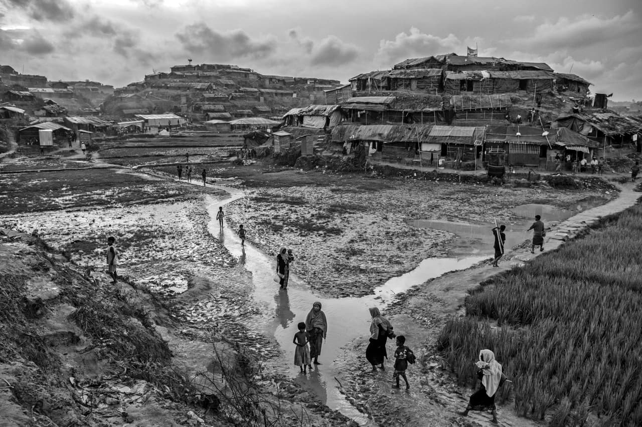 Mujeres y niños rohingya caminan por las callejuelas inundadas de un extenso campo de refugiados en Baluki, en Cox’s Bazar, Bangladesh. Myanmar, país mayoritariamente budista, no reconoce a los rohingya como ciudadanos y los considera ilegales.
