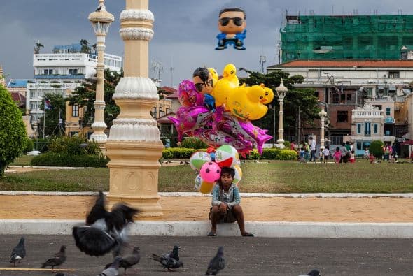 Un niño vendedor de globos se sienta a mirar a las palomas frente al Palacio Real de Camboya.