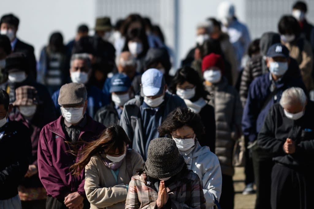 Personas con mascarillas oran por las víctimas del terremoto y tsunami en Japón en 2011.