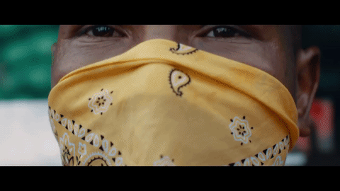 Dos chicos cubriéndose el rostro con paliacates detrás de un camión mientras alguien baila en el interior.