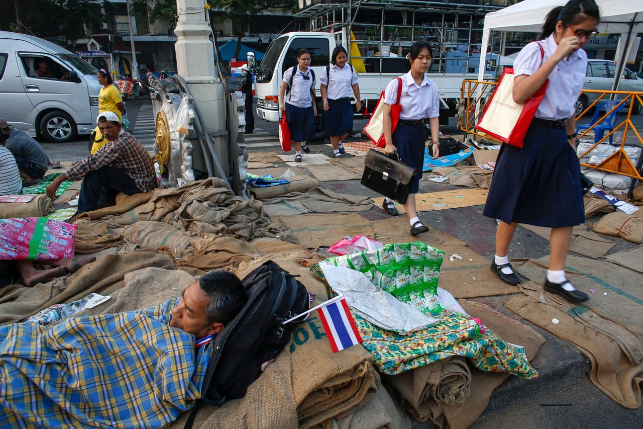 <b>Tailandia.</b> Estudiantes de camino a la escuela deben pasar frente manifestantes contra el gobierno acostados en el suelo en el monumento a la democracia de Bangkok. 11 de diciembre de 2013