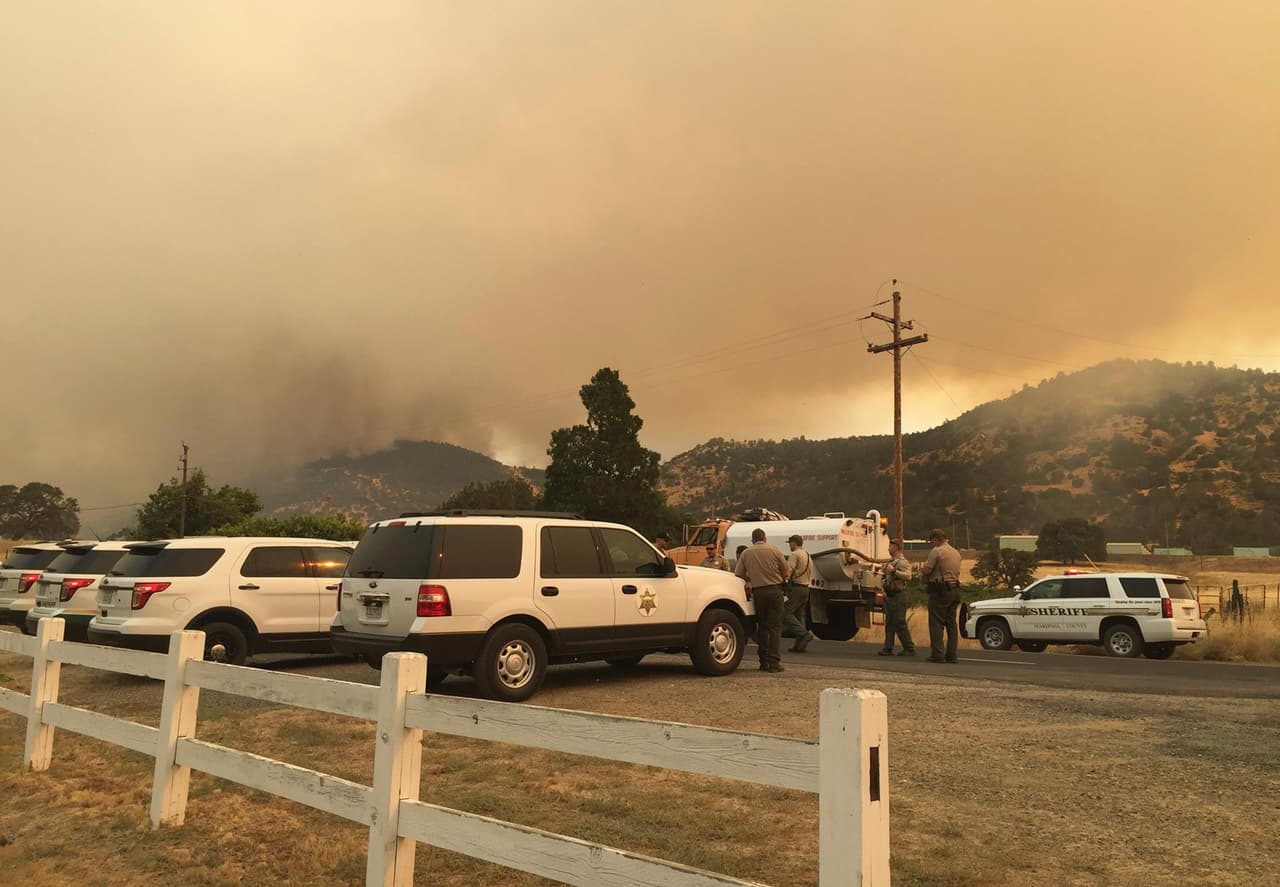 Los miembros de la Oficina del Sheriff de los condados de Merced y Mariposa se reúnen con el humo del incendio sobre sus cabezas, oeste de la reserva forestal Yosemite.