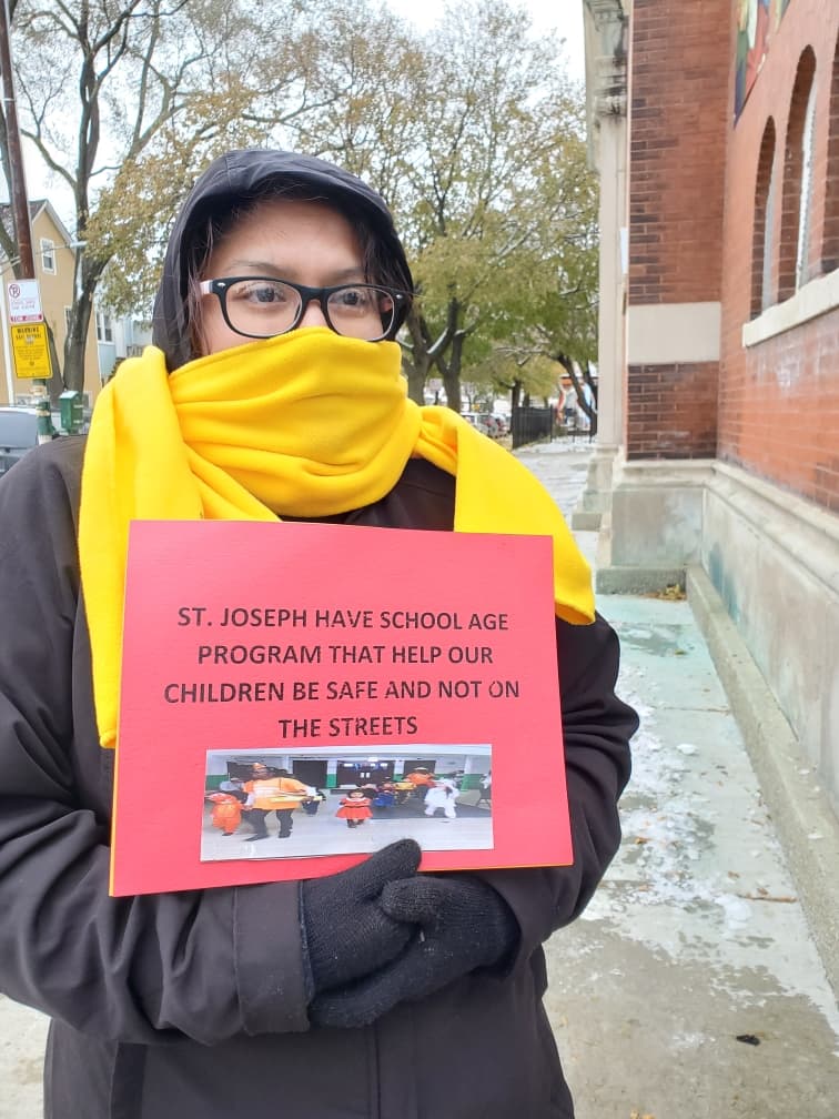 El póster que esta madre sostiene dice,
<i> "St. Joseph tiene un programa para niños que los mantiene seguros y fuera de la calles". </i>