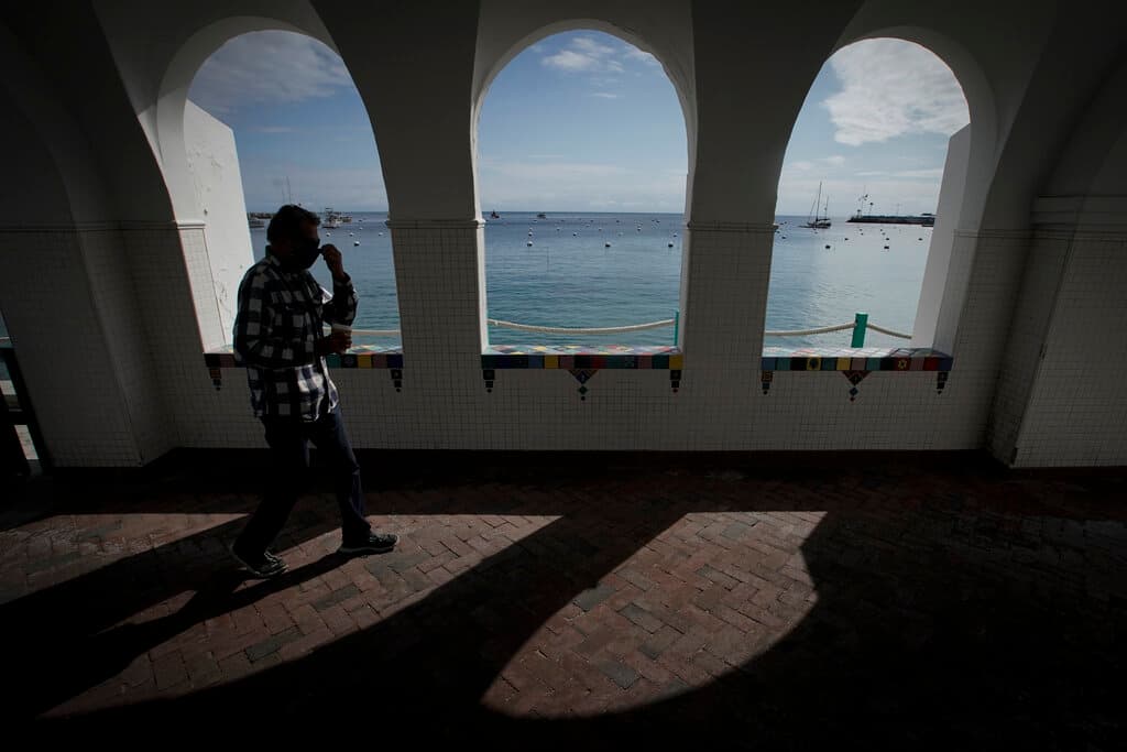 Un hombre se ajusta su máscara mientras camina junto a la bahía de la isla de Santa Catalina, en California, el 18 de abril del 2020. (AP Foto/Chris Carlson)
