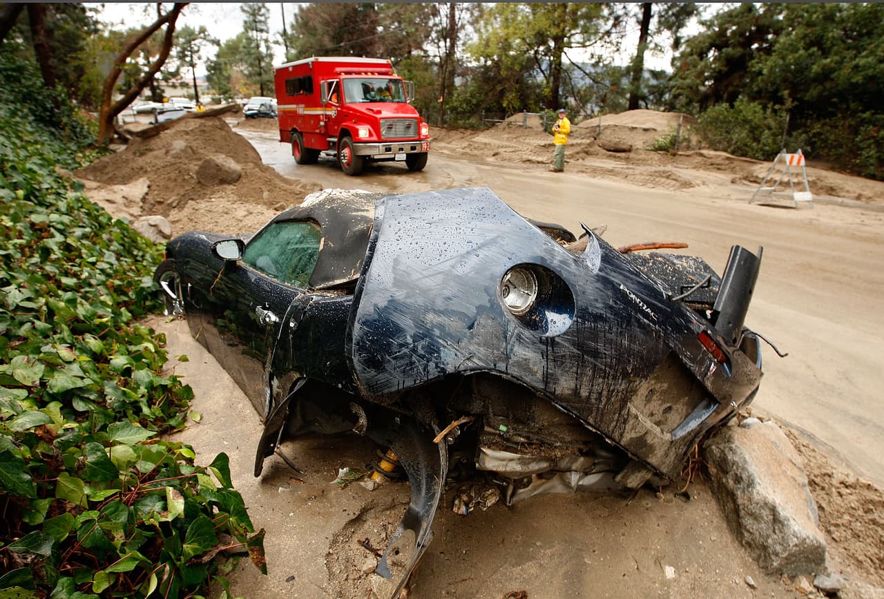 LA CANADA-FLINTRIDGE, CA - FEBRUARY 6: Firefighters drive by a mangled Pontiac car that was swept away by debris flows that damaged homes on February 6, 2010 in La Canada Flintridge, California. Large wildfires in 2008 and 2009 stripped the hills and mountains of vegetation, resulting in mud and debris flow danger as winter rains pass over foothill communities where thousands of people have been evacuated at times in recent weeks. The threat is particularly high near the San Gabriel Mountains above La Canada-Flintridge area which were denuded of natural flood-controlling vegetation by the 250-plus square mile Station. At least 40 homes have been severely damaged and 500 remain evacuated. (Photo by David McNew/Getty Images)