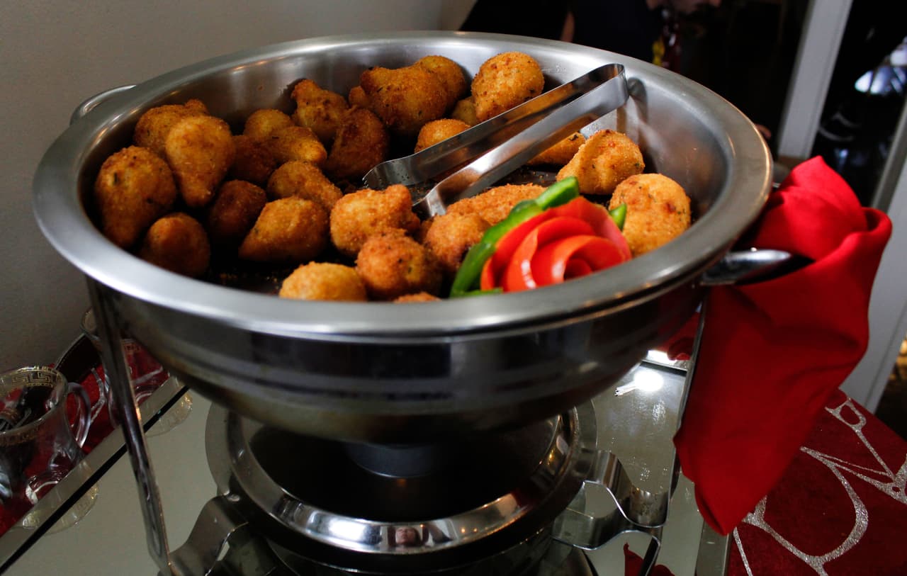 Una charola repleta de “coxinha”—bolitas de masa fritas y rellenas de pollo o queso—se ofrecen como aperitivo mientras los clientes esperan a sentarse para degustar el menú tradicional de Sinhá. 
<br>
<br>