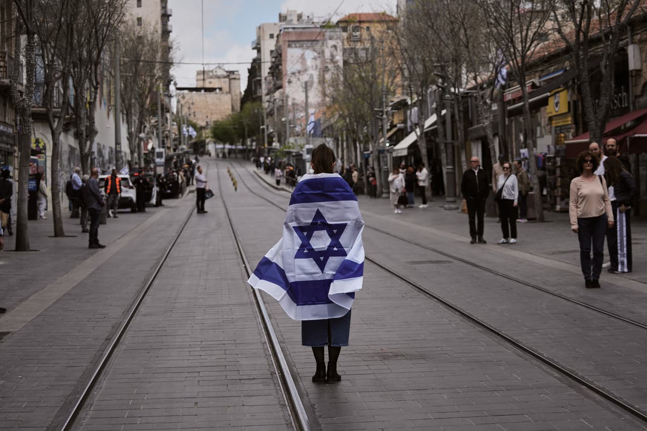 <br>Una mujer envuelta en una gran bandera permanecía inmóvil en medio de las vías del tren ligero en una calle vacía de Jerusalén, en señal de silencio nacional. 
<br>