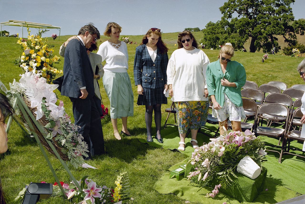 Guillermo Andrade (izq.) y amigos de la familia visitan la tumba de sus dos hijas a un año de la tragedia, en 1994, luego de los servicios fúnebres en California. Sus dos hijas y una nieta estuvieron entre los casi 80 seguidores del culto que murieron en el incendio que destruyó el complejo.