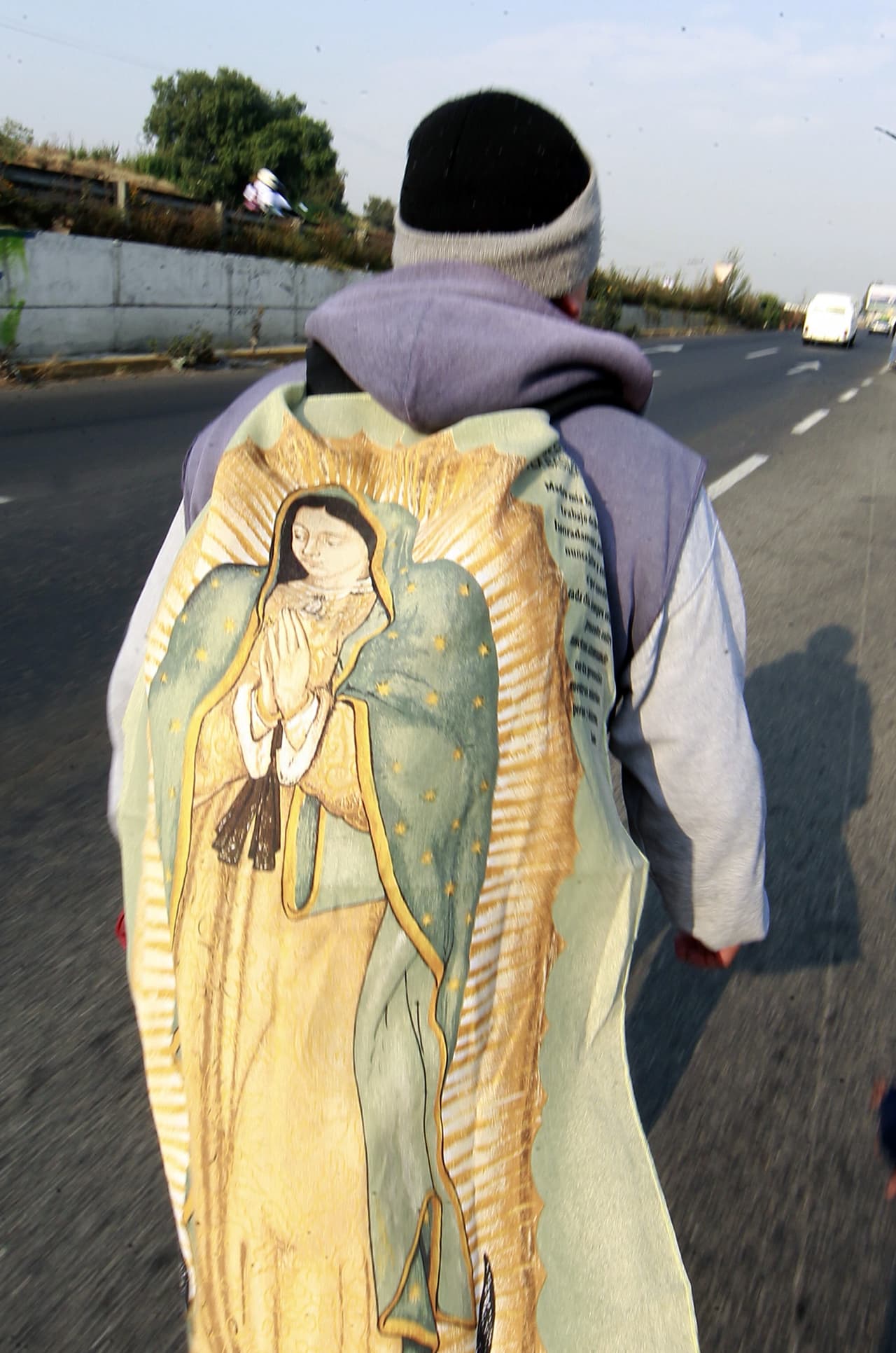 Peregrino camina en la carretera rumbo al DF con una imagen de la Virgen sobre su espalda.
