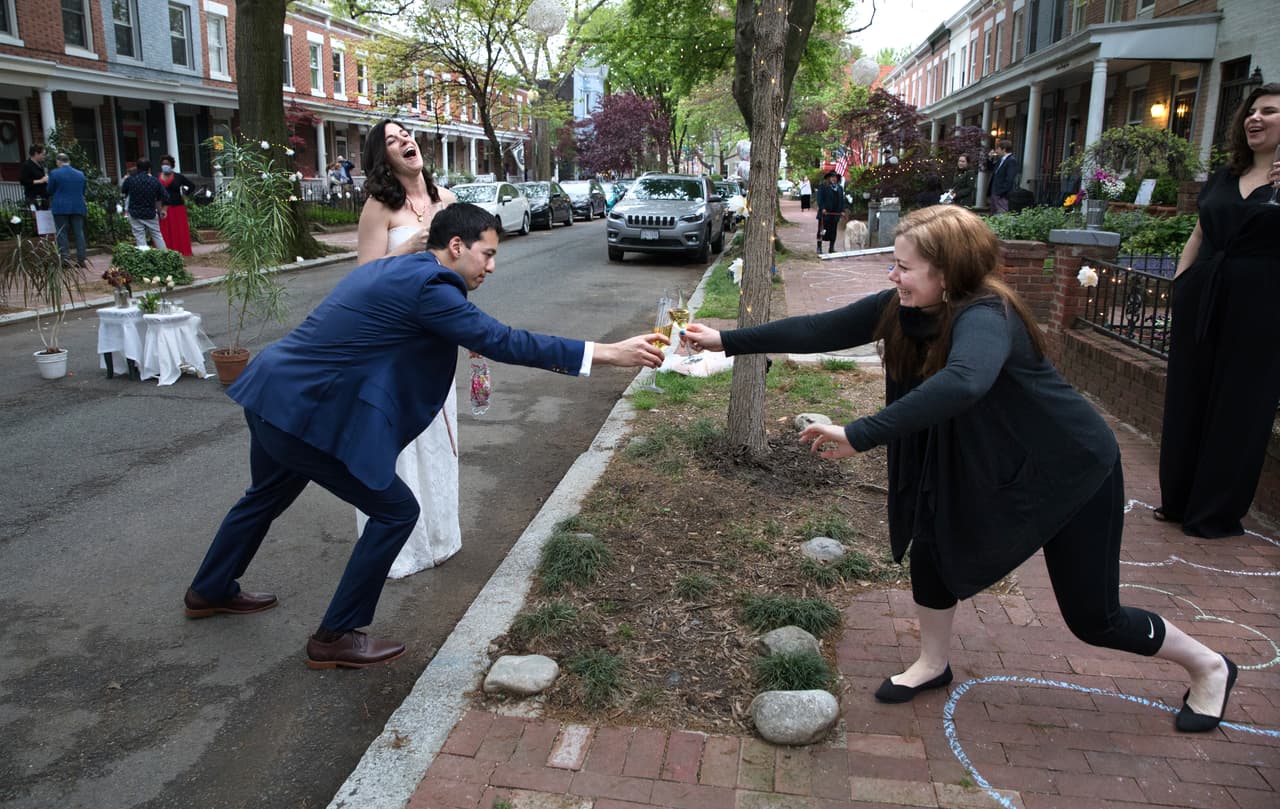 <b>Boda con distancia e invitados virtuales.</b> Una pareja brinda con sus vecinos durante su matrimonio en una calle de Capitol Hill, Washington D.C. Los novios celebraron con algunos vecinos pero sus sus familiares y amigos estuvieron presentes en la ceremonia vía Zoom.
<br>