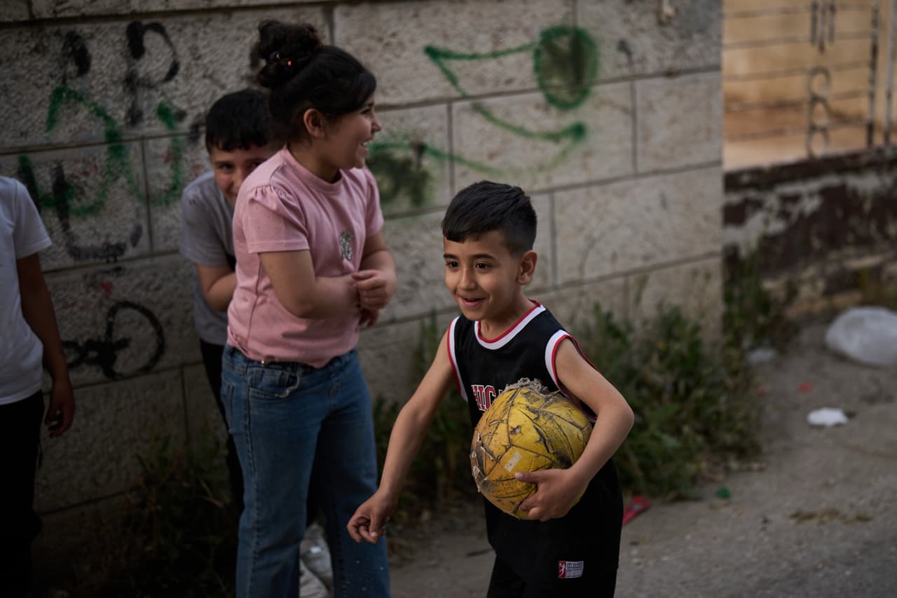 Un niño palestino lleva un balón de fútbol desgastado mientras juega con sus amigos en un callejón de la ciudad de Al-Ram, en Cisjordania, el lunes 11 de mayo de 2026. (Foto AP/Leo Correa)