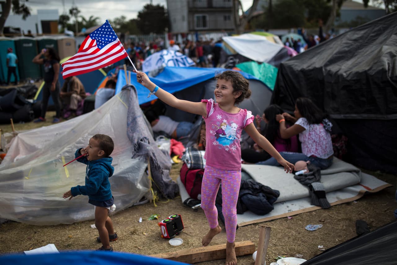 <b>Saludo con la bandera.</b> Más de 5,000 migrantes, muchos de ellos niños, vivieron varias semanas en un refugio con sanitarios portátiles desbordados y un enorme charco de agua sucia que crecía cada vez que alguien tomaba una ducha.
<a href="https://www.univision.com/noticias/inmigracion/aguantar-o-volver-las-condiciones-infrahumanas-que-soportan-los-migrantes-en-el-refugio-colapsado-de-tijuana-fotos-fotos">Las condiciones deplorables de la Unidad Deportiva Benito Juárez, donde fueron alojados la mayoría de los centroamericanos, impulsaron a algunos a regresar a sus países o a buscar ingresar a EEUU ilegalmente.</a> En la fotografía, tomada el 24 de noviembre de 2018, la pequeña hondureña Génesis Belén Mejía Flores saluda a un helicóptero estadounidense que volaba cerca del albergue, ubicado al norte de Tijuana.