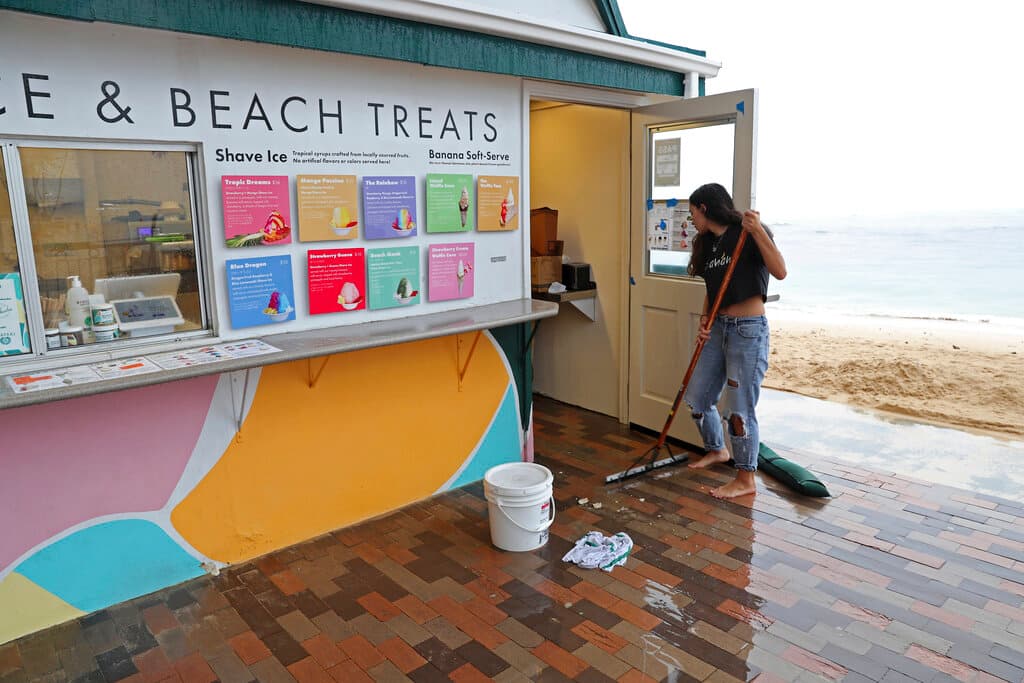 Calista Cafiero barre el agua de la tormenta fuera de la tienda que administra en la playa de Waikiki, el lunes 6 de diciembre de 2021, en Honolulu. Cafiero dijo que la tormenta inundó la tienda.