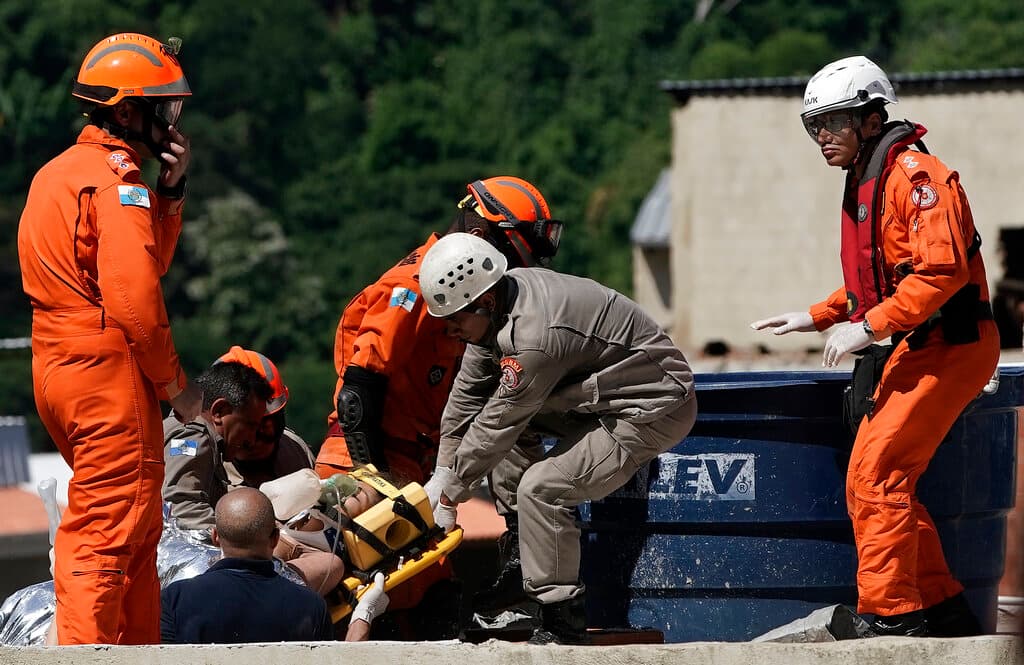 Bomberos sacan en camilla a una mujer rescatada de los escombros.