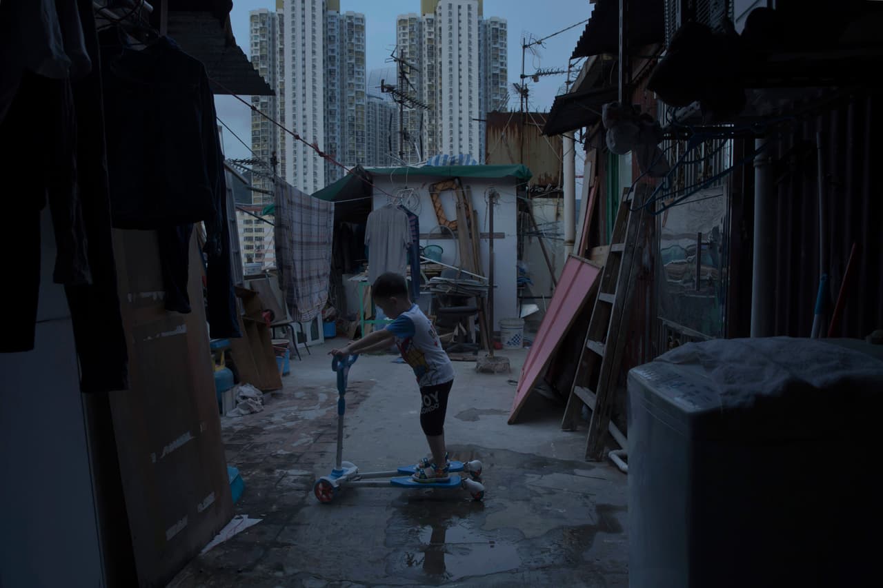 Un niño de cinco años juega fuera de su pequeña casa de hormigón y metal corrugado en la terraza de un bloque de apartamentos. Vive con sus padres en una choza ilegal en la azotea, al lado de una urbanización pública de Hong Kong.