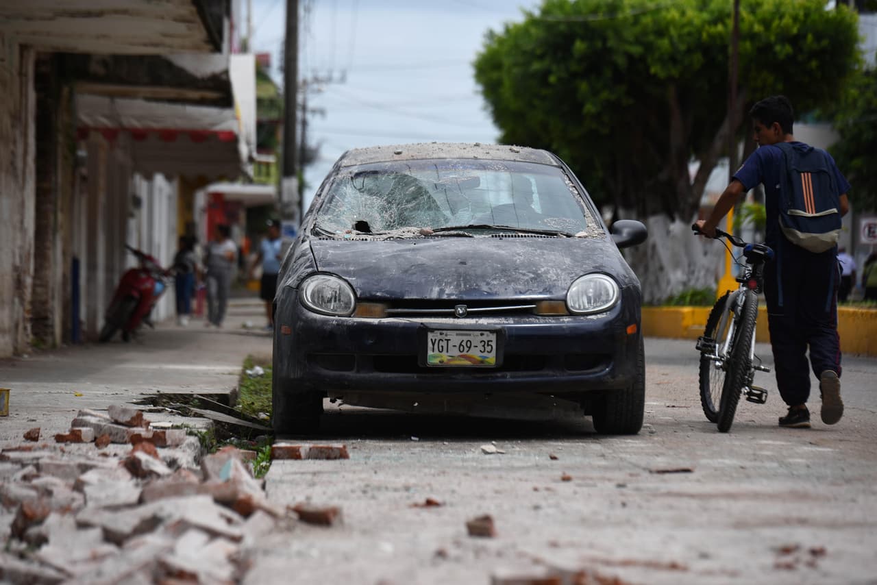 Un ciclista pasa junto a un vehículo averiado por objetos que le cayeron por un sismo en el municipio de Matías Romero, en el estado mexicano de Oaxaca (México).