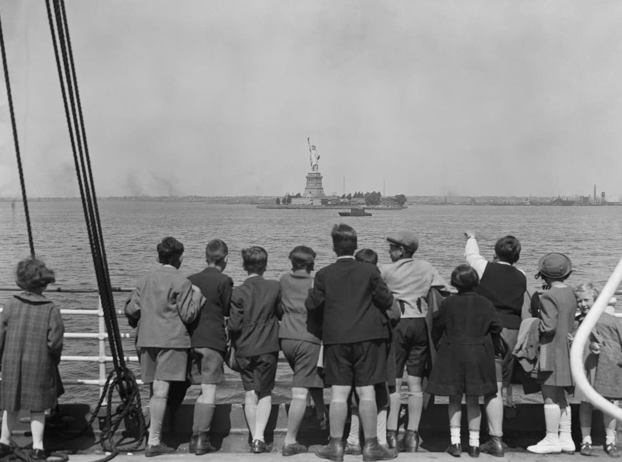 Un grupo de niños refugiados de la Alemania Nazi llegando al puerto de Nueva York a mediados del siglo XX. En 1892 la vecina Ellis Island se convirtió en la principal estación de inmigración del país, y la imponente figura de la Estatua de la Libertad recibió a más de 12 millones de extranjeros buscando refugio en las seis décadas siguientes.
<br>