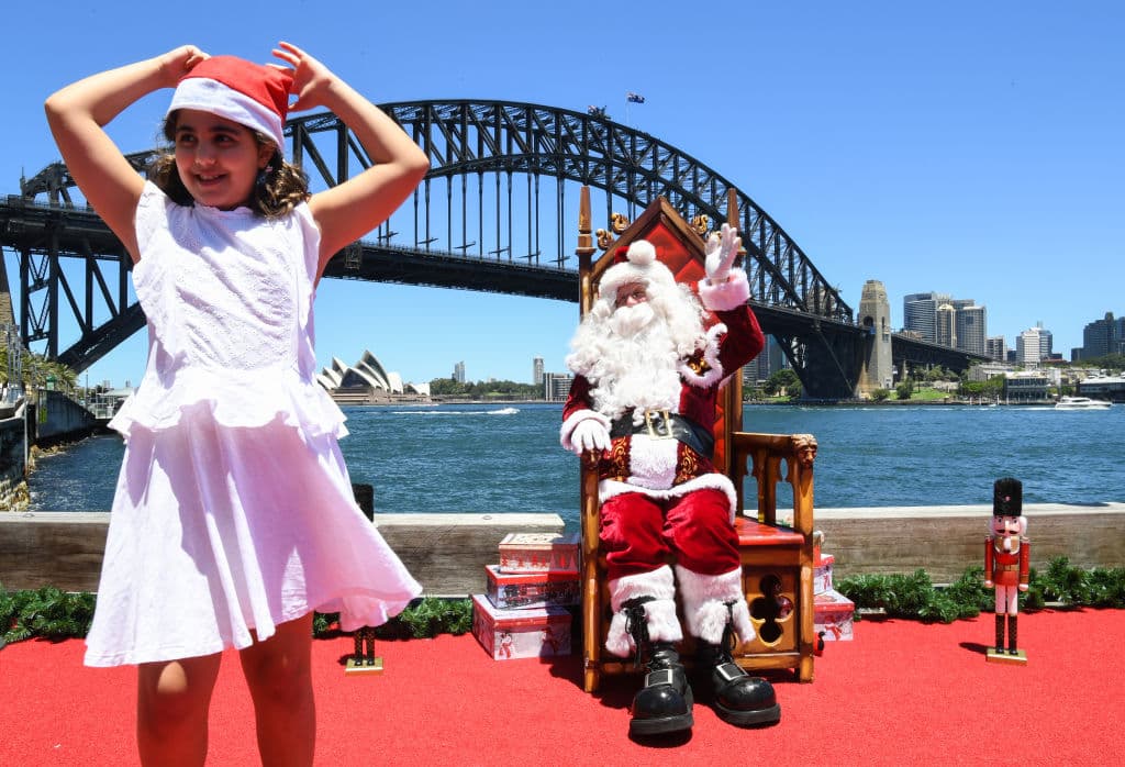 Santa Claus posa para los fotógrafos desde el Luna Park de Sydney, Australia, este 24 de diciembre. Cientos de locales y visitantes han tenido la oportunidad de tomarse una fotógrafía con el fondo icónico del Harbour Bridge y la Opera House.