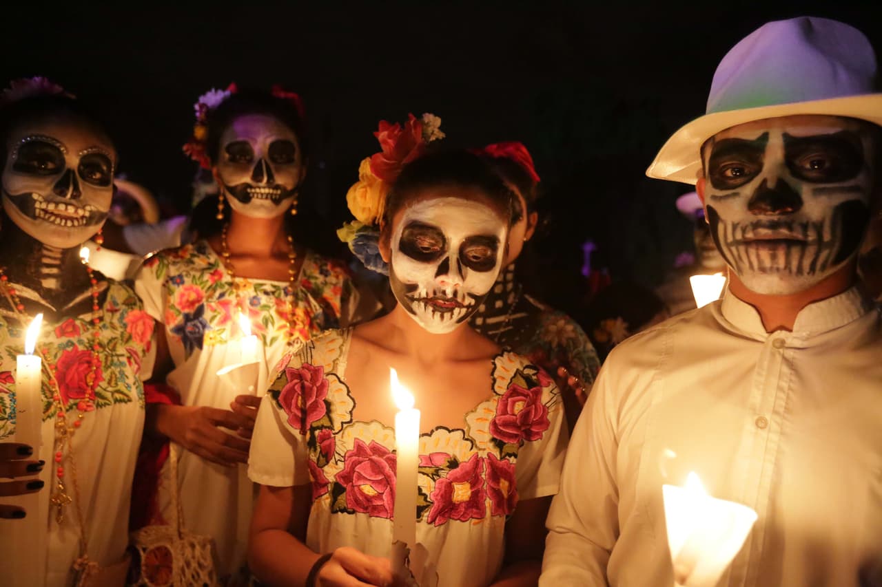 Hombres y mujeres de Mérida caminan por las calles con trajes tradicionales y rostros pintados de calavera.