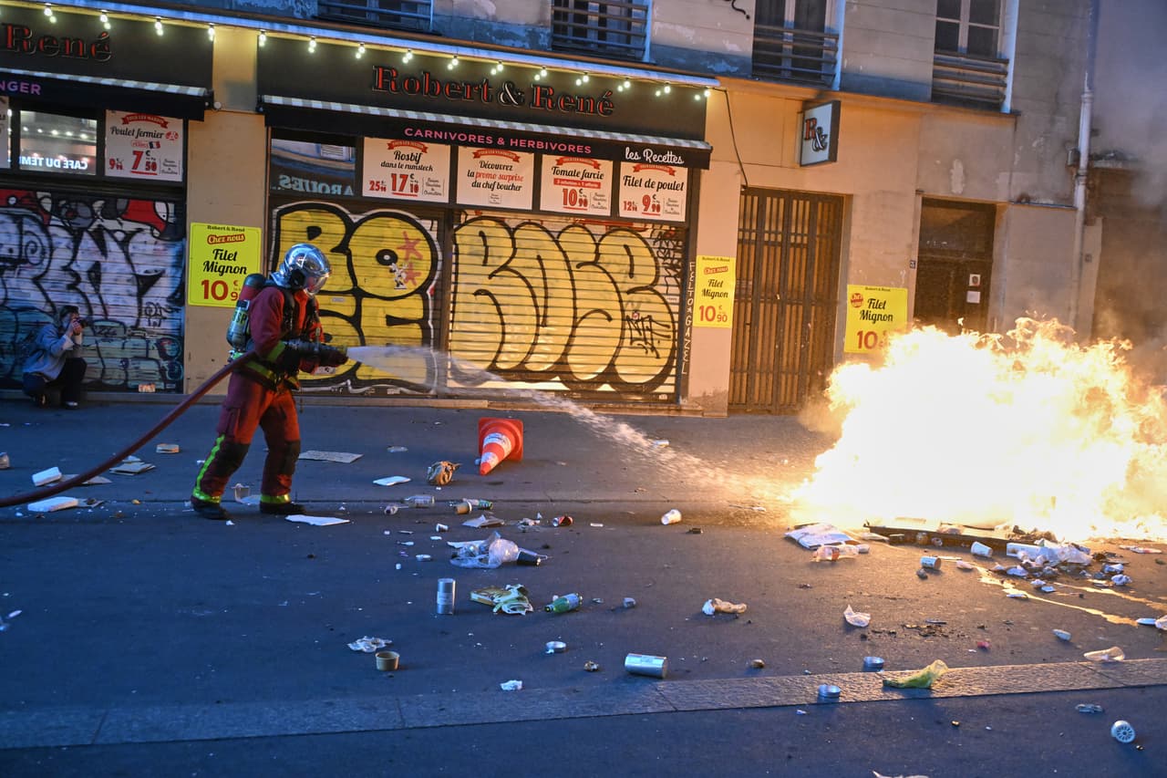 Un bombero extingue un incendio durante enfrentamientos con la policía un día después de una manifestación contra el aumento del costo de vida, sumándose a las quejas de los estudiantes, en París, el domingo 18 de octubre de 2026.