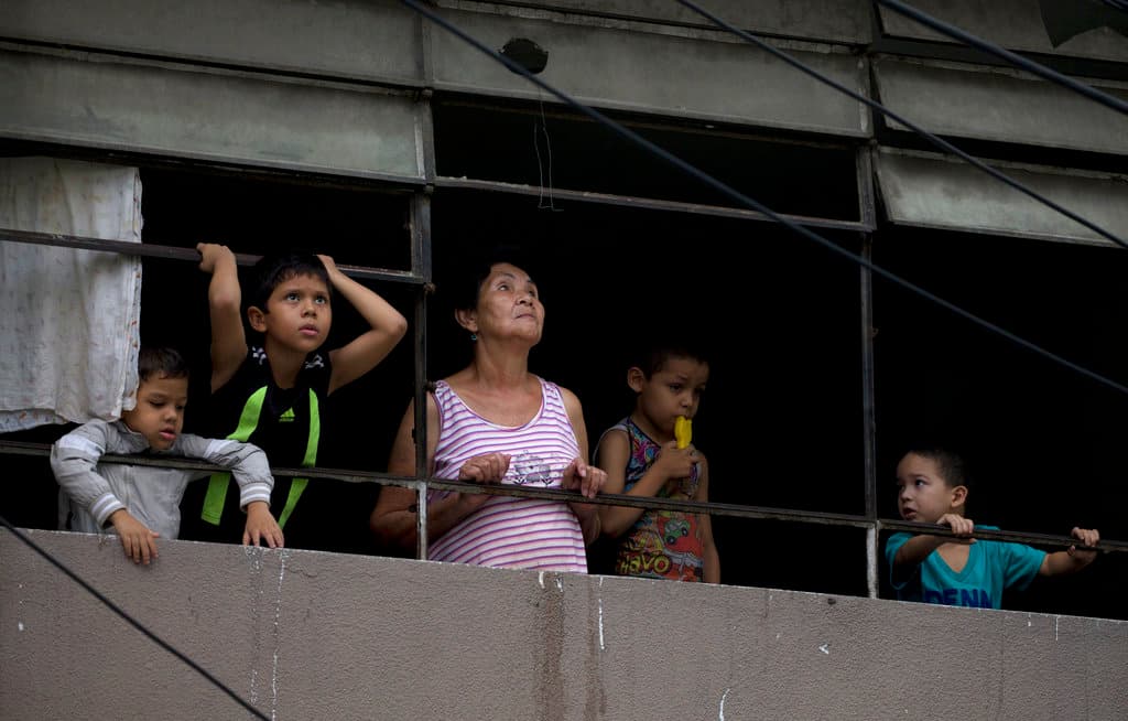 Una mujer y unos niños observan desde la ventana de su apartamento un rascacielos abandonado e inacabado conocido como "La Torre de David", que presenta una inclinación en los pisos superiores, un día después de un potente terremoto, en Caracas, Venezuela, el miércoles 22 de agosto de 2018.