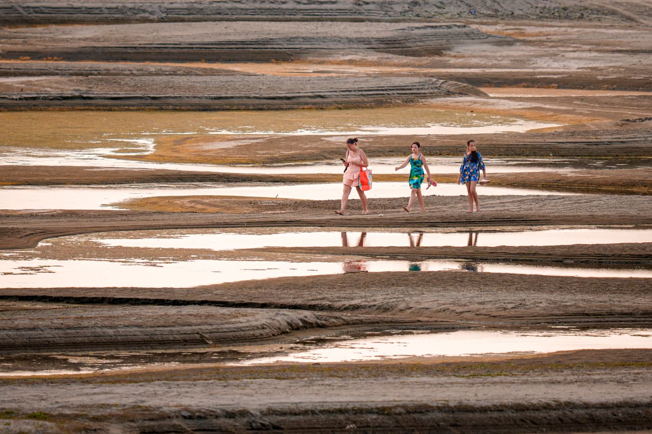 Unas personas caminan sobre un banco de arena en el río Danubio, donde zonas habitualmente sumergidas han quedado al descubierto debido a los niveles de agua excepcionalmente bajos, en Rasova, Rumanía, el viernes 7 de agosto de 2026.