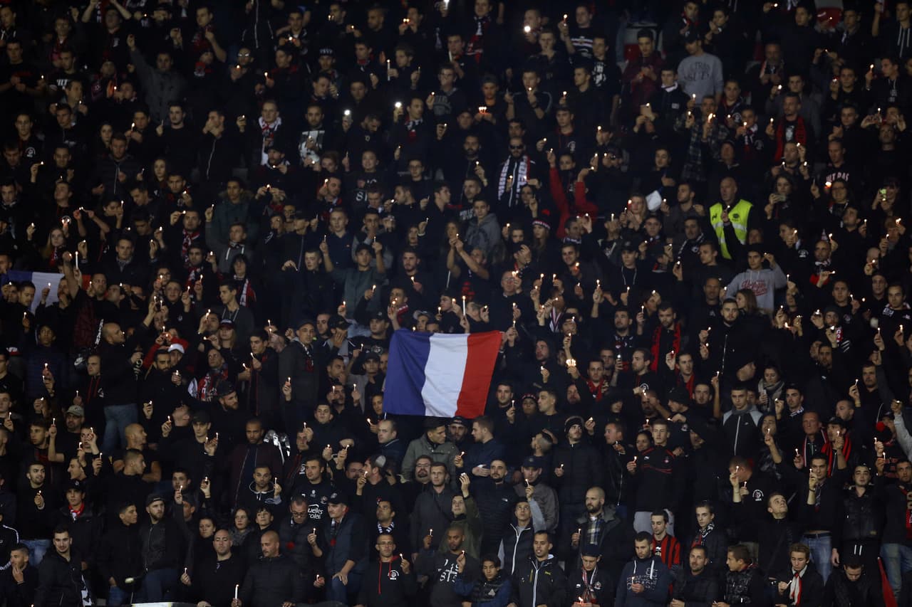 Seguidores del equipo de la liga francesa Nice sostienen velas y la bandera del país al guardar un minuto de silencio por los ataques.
