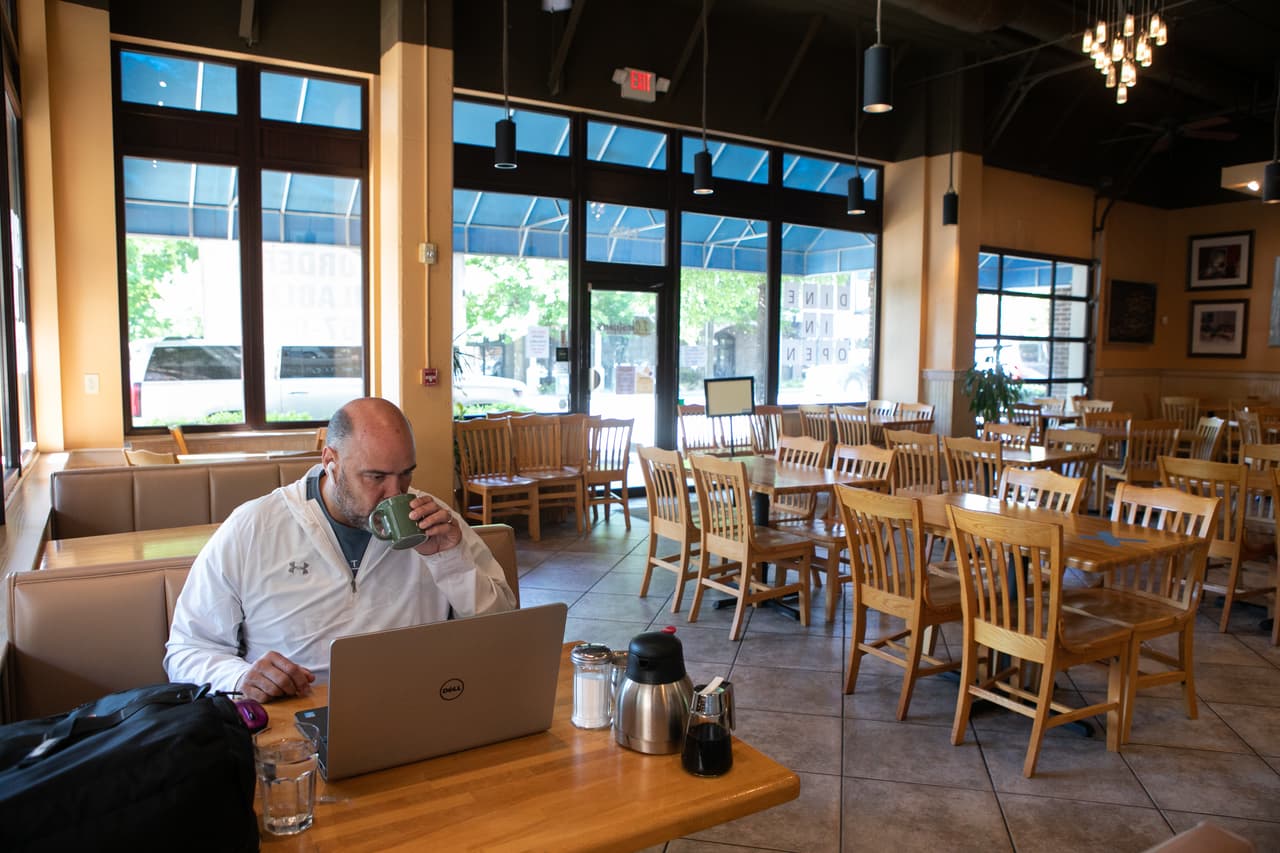 Duke Scott trabaja de forma remota en el comedor vacío del restaurante J. Christopher's el 27 de abril de 2020 en Brookhaven, Georgia. Las tablas están marcadas con una "X" para que los clientes no las usen para adherirse a los protocolos de distanciamiento social.