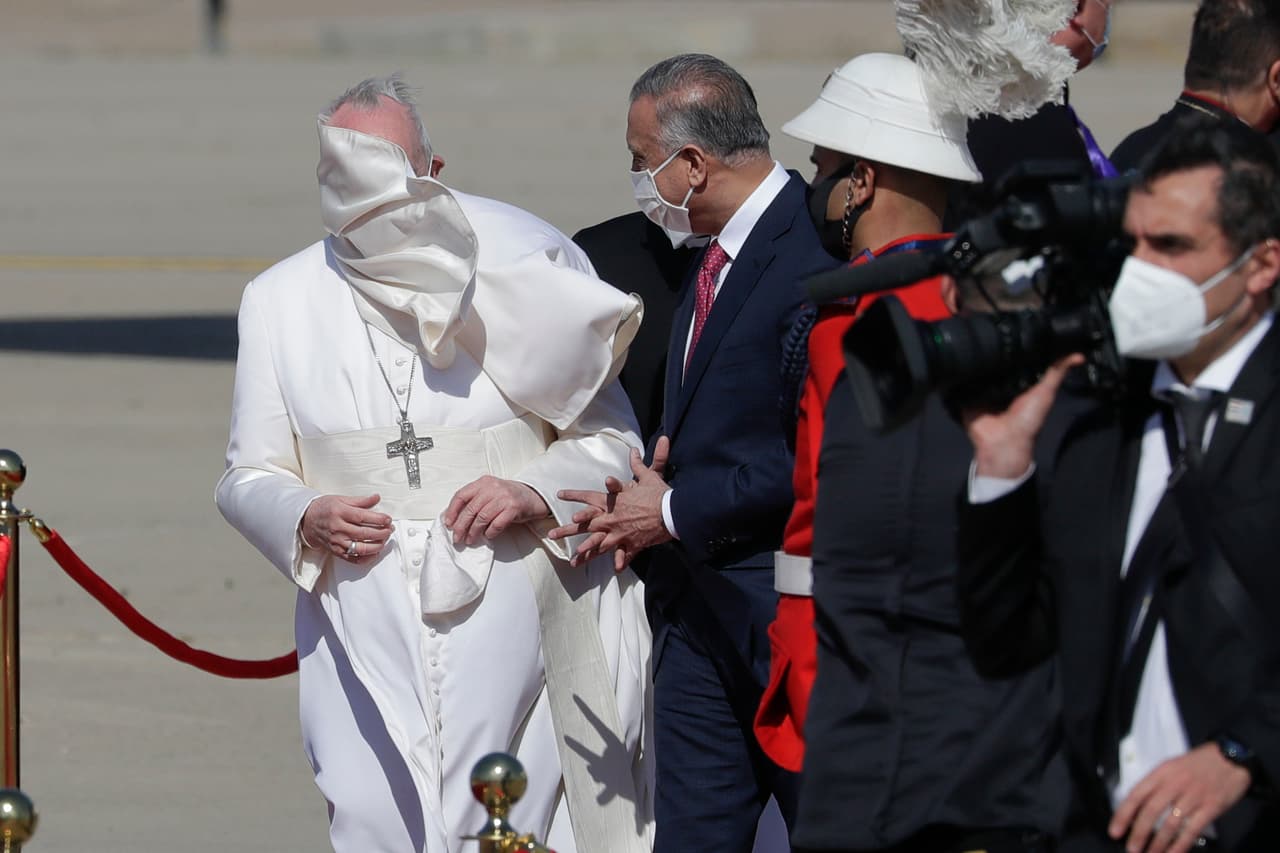 Una ráfaga de viento sopla el manto del papa Francisco mientras está junto al primer ministro iraquí Mustafa al-Kadhimi a su llegada al aeropuerto internacional de Bagdad.