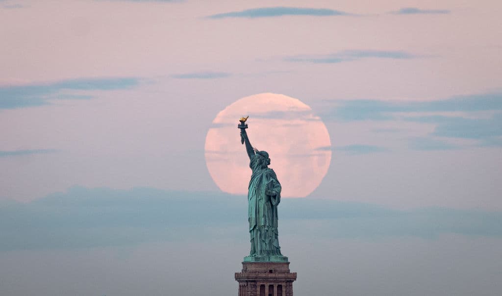 La luna llena de mayo de 2020, conocida como a Luna llena de flores, es la última Superluna de una serie de cuatro comenzada en febrero. En la foto, así se vio el astro detrás la Estatua de la Libertad, este 7 de mayo de 2020 en la ciudad de Nueva York.
<b> La <a href="https://solarsystem.nasa.gov/news/1220/the-next-full-moon-is-a-supermoon-flower-moon/" target="_blank">NASA</a> señala además que la Luna llena de mayo se le llama Luna Madre, Luna de Leche y Luna de Maíz, dependiendo las tradiciones de diferentes pueblos. </b>