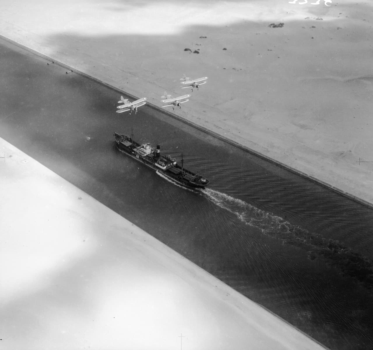 A partir de 1876 comenzaron a hacerse mejoras importantes del canal, ampliaciones, profundizaciones y se construyeron nuevas bahías y desvíos. Esta fotografía muestra un carguero escoltado por aviones de la Fuerza Aérea Real británica, en marzo de 1938.
<br>