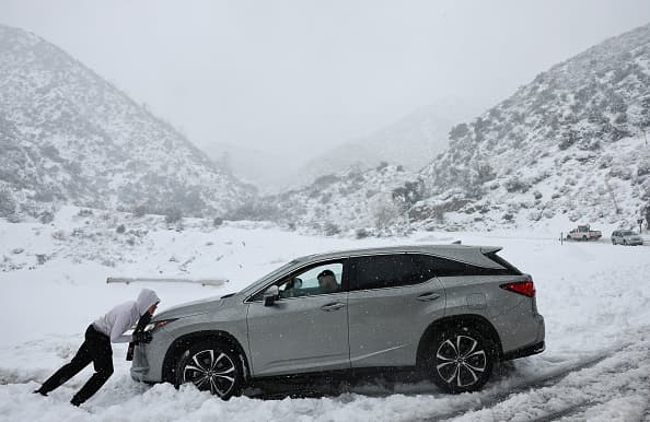 Una persona empujando su vehiculo en medio de la poderosa tormenta invernal que azota el Sur de California.