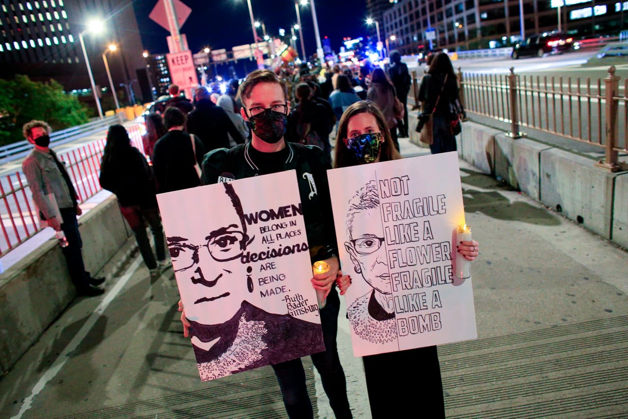 La gente sostiene banderas mientras marchan por el puente de Brooklyn mientras presentan sus respetos a la juez Ginsburg.