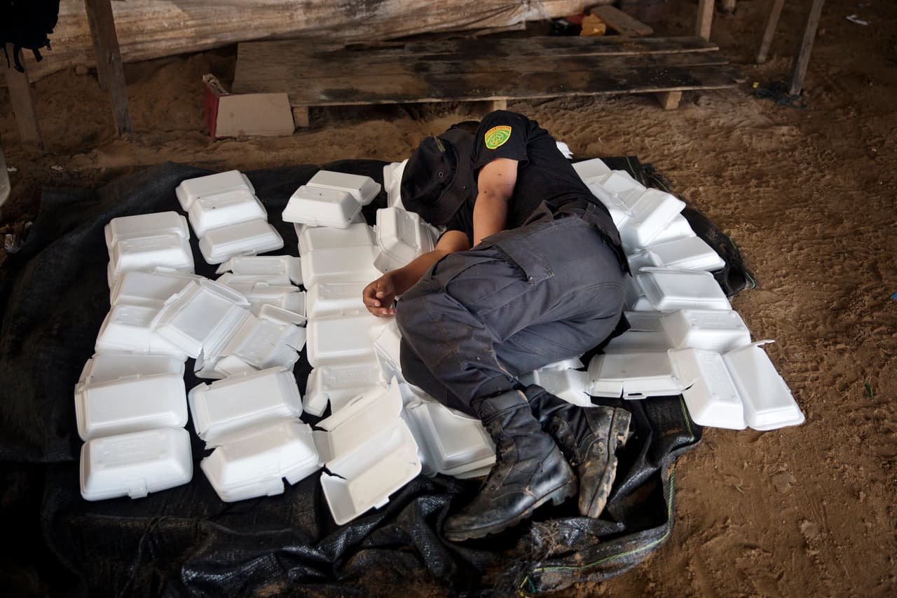 Un oficial de la policía duerme en cajas de alimentos desechados dentro de un campo utilizado para la extracción ilegal de oro.