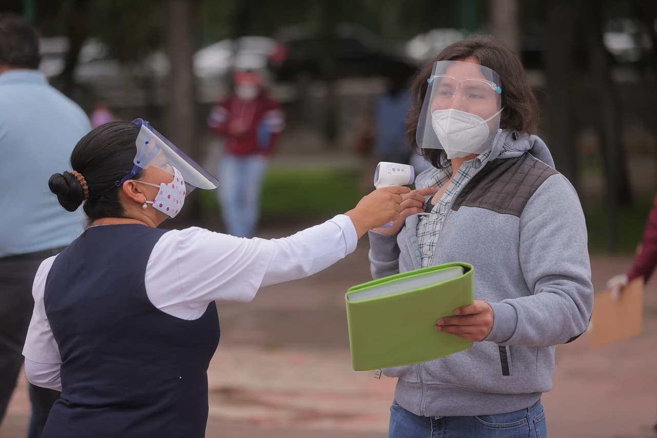 Un miembro del personal de la UNAM mide la temperatura corporal de un estudiante antes de ingresar al examen de admisión. 
<b>Fue la primera vez en muchos años que el Estadio Olímpico es utilizado para la prueba, en parte porque los expertos consideran que es más difícil contagiarse con el virus en un espacio al aire libre.</b>