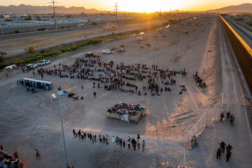 Sale el sol y los migrantes esperan organizados fuera de las vayas fronterizas para entrar a El Paso, Texas.