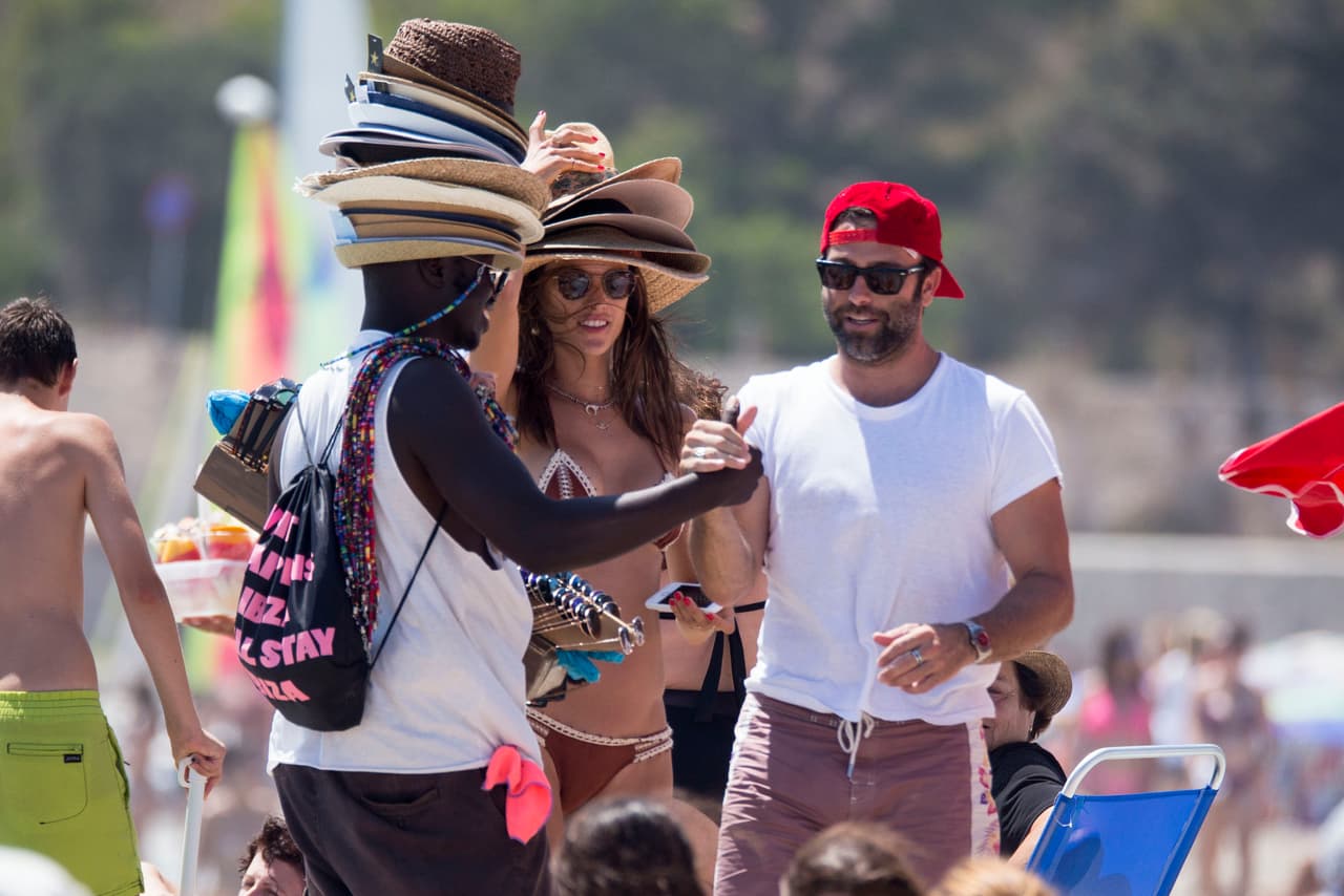 Alessandra Ambrosio lleva más de una semana en las playas de Ibiza disfrutando del verano español. Aquí, la modelo de 36 años bromea con un vendedor de sombreros en la playa.