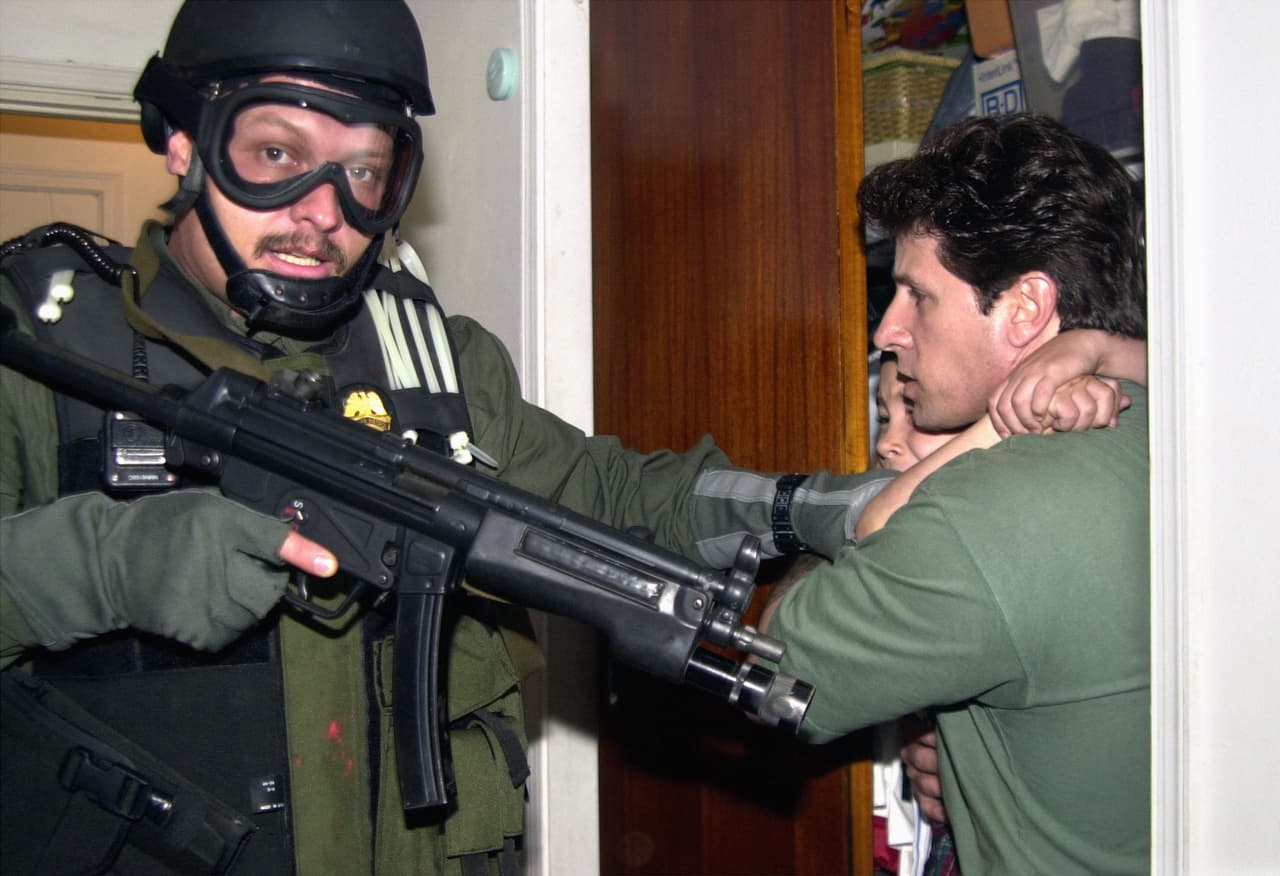 Es la quinta fotografía de las siete que logró tomar de ese momento. Afuera un grupo de vecinos trataba de evitar que se llevaran al niño. La familia en Miami alegaba que el deseo de la madre de Elián era que el niño viviera en Miami. Pero perdieron el juicio.