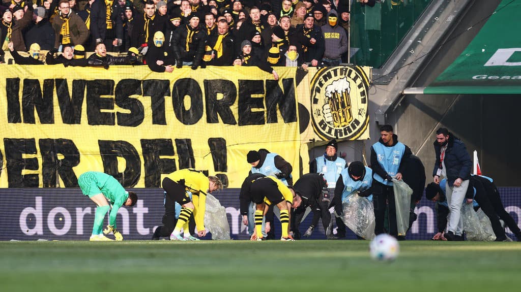 Aficionados lanzan monedas en protesta en Alemania; jugadores limpian campo