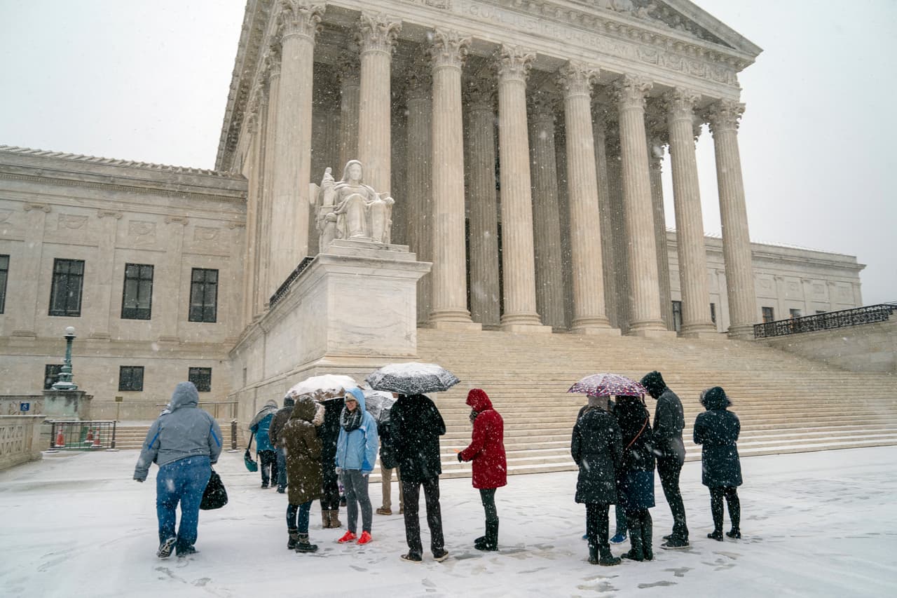 Un grupo de visitantes aguarda en las afueras del edificio de la Corte Suprema, en Washington, donde cayó una copiosa nevada este miércoles.