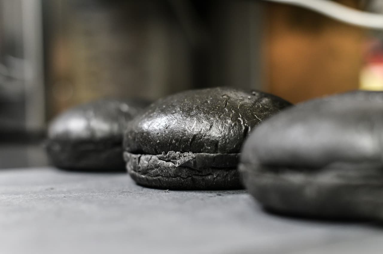 La hamburguesa original lleva dos tajadas de pan negro, carne, una lasca de queso también de color negro.