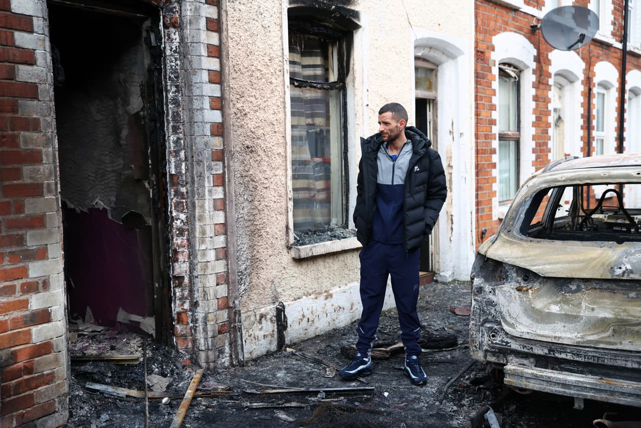 Jamie Corrie permanece junto a su casa calcinada tras el estallido de disturbios a última hora del martes en el este de Belfast. (Foto AP/Peter Morrison)