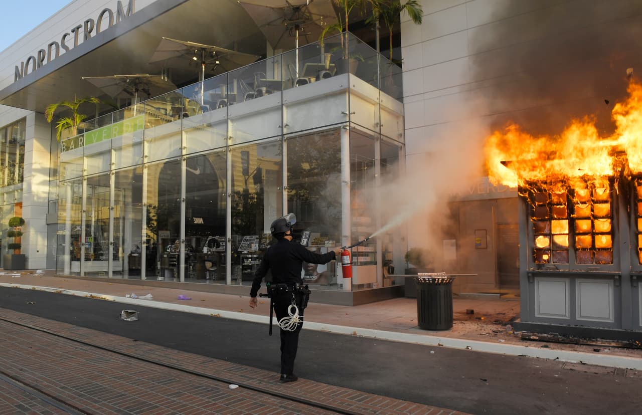 En la misma zona, un oficial de policía intenta apagar un quiosco del Departamento de Policía de Los Ángeles que fue incendiado en el centro comercial The Grove.