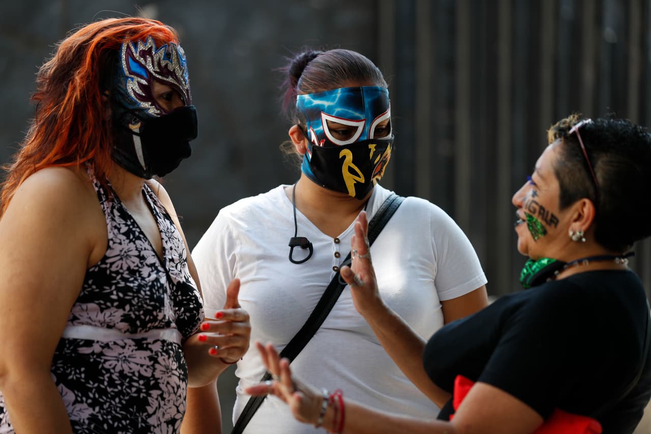 Fue a finales de marzo cuando el gobierno de la Ciudad de 
<a href="https://www.univision.com/temas/mexico-city">México</a> 
<b>decretó el cierre de estadios, gimnasios y centros deportivos, lo que provocó el desempleo de cientos de luchadores.</b>
<br> 
<br>Las gladiadoras Migala, Skarlet y La Zorra, conversan mientras esperan en la fila para recibir su despensa.