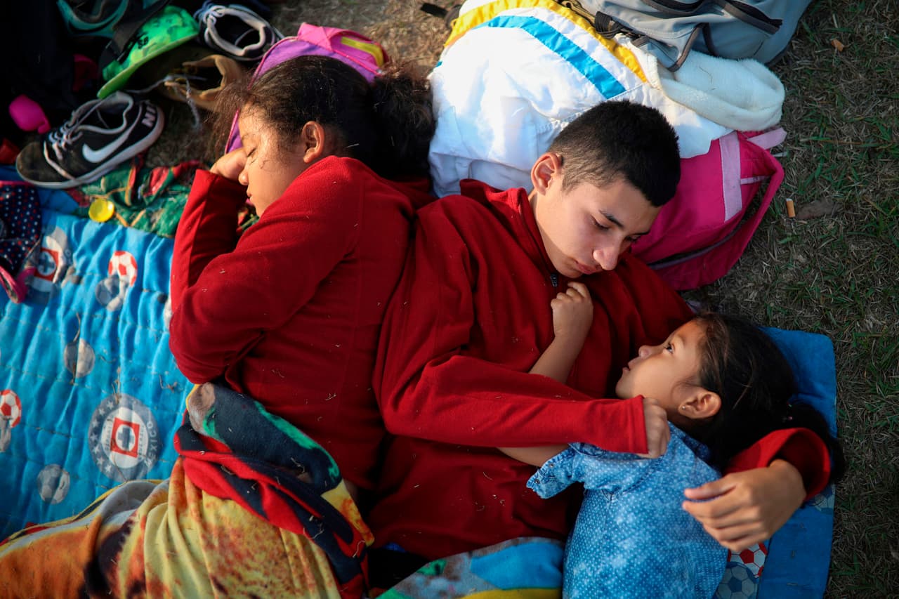 In this April 4, 2018 photo, the Zelaya siblings, from El Salvador, Nayeli, right, Anderson, center, and Daniela, huddle together on a soccer field, at the sports club where Central American migrants traveling with the annual "Stations of the Cross" caravan are camped out, in Matias Romero, Oaxaca State, Mexico. The children's father Elmer Zelaya, 38, said the family is awaiting temporary transit visas that would allow them to continue to the U.S. border, where they hope to request asylum and join relatives in New York.(AP Photo/Felix Marquez)