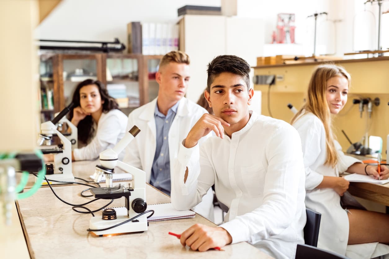 Group of high school student with microscopes in laboratory during biology class.