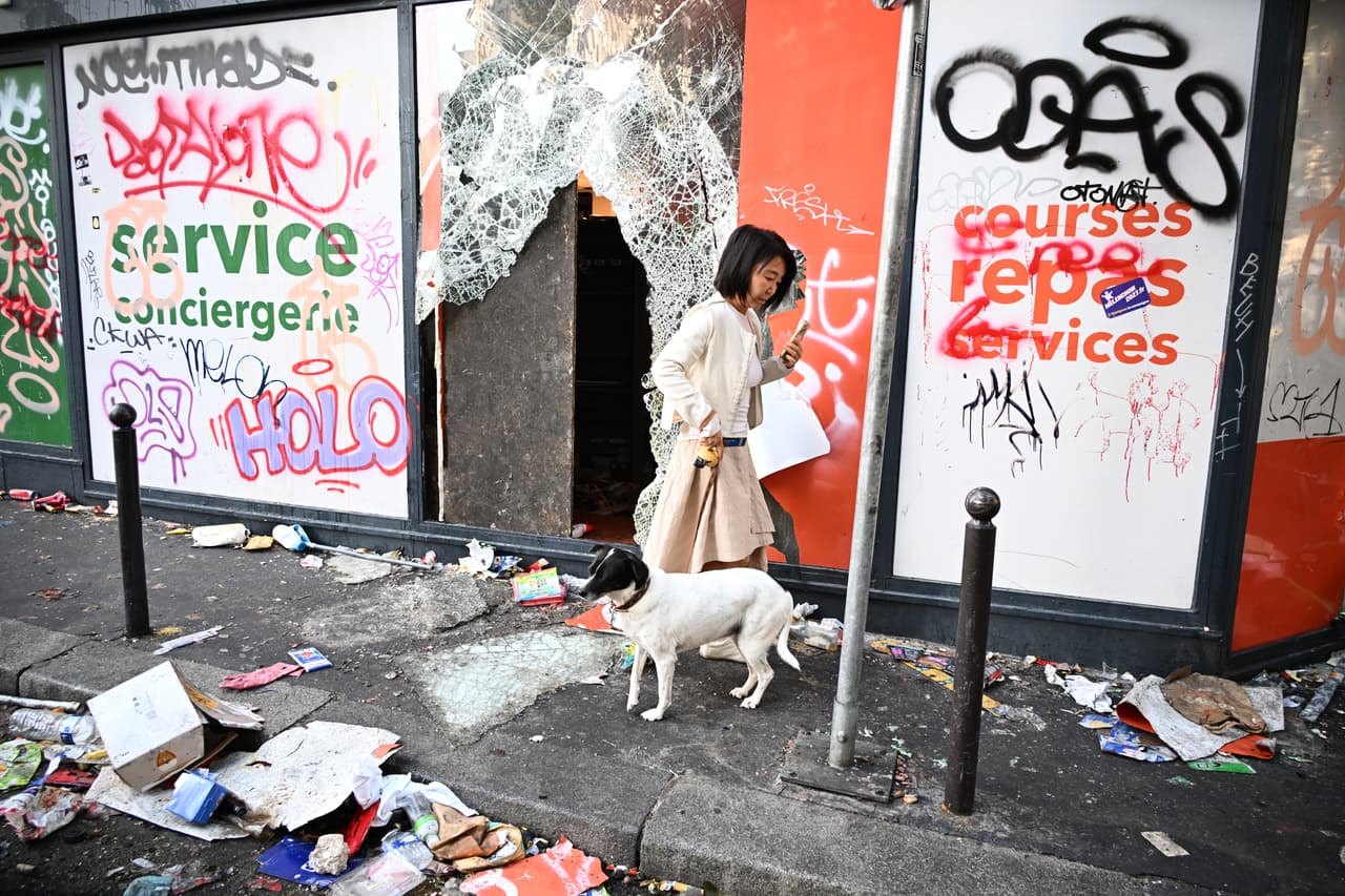 Una mujer pasea a su perro frente a una tienda saqueada al día siguiente de una manifestación.