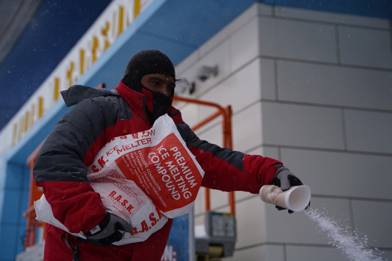 Un trabajador arroja sal al pavimento para derretir el hielo en el centro de Indianápolis.