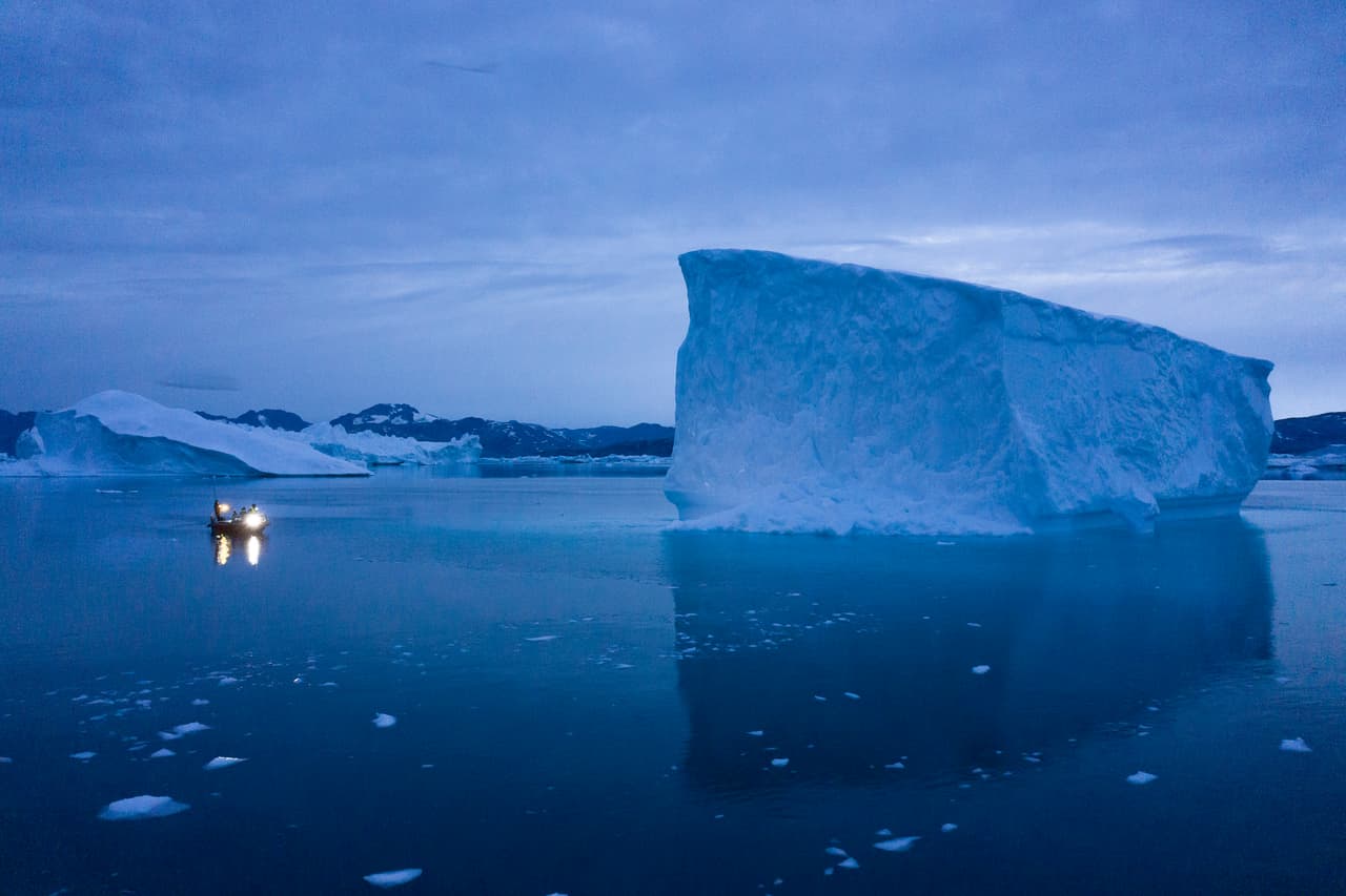 Una embarcación navega por la noche muy cerca de glaciares enormes, en el este de Groenlandia.