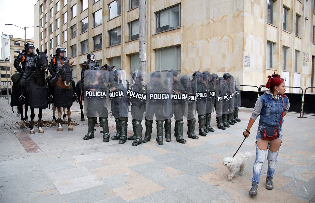 Una mujer camina con su mascota en frente de un grupo de policías antidisturbios durante una manifestación del Primero de Mayo en Bogotá, Colombia.